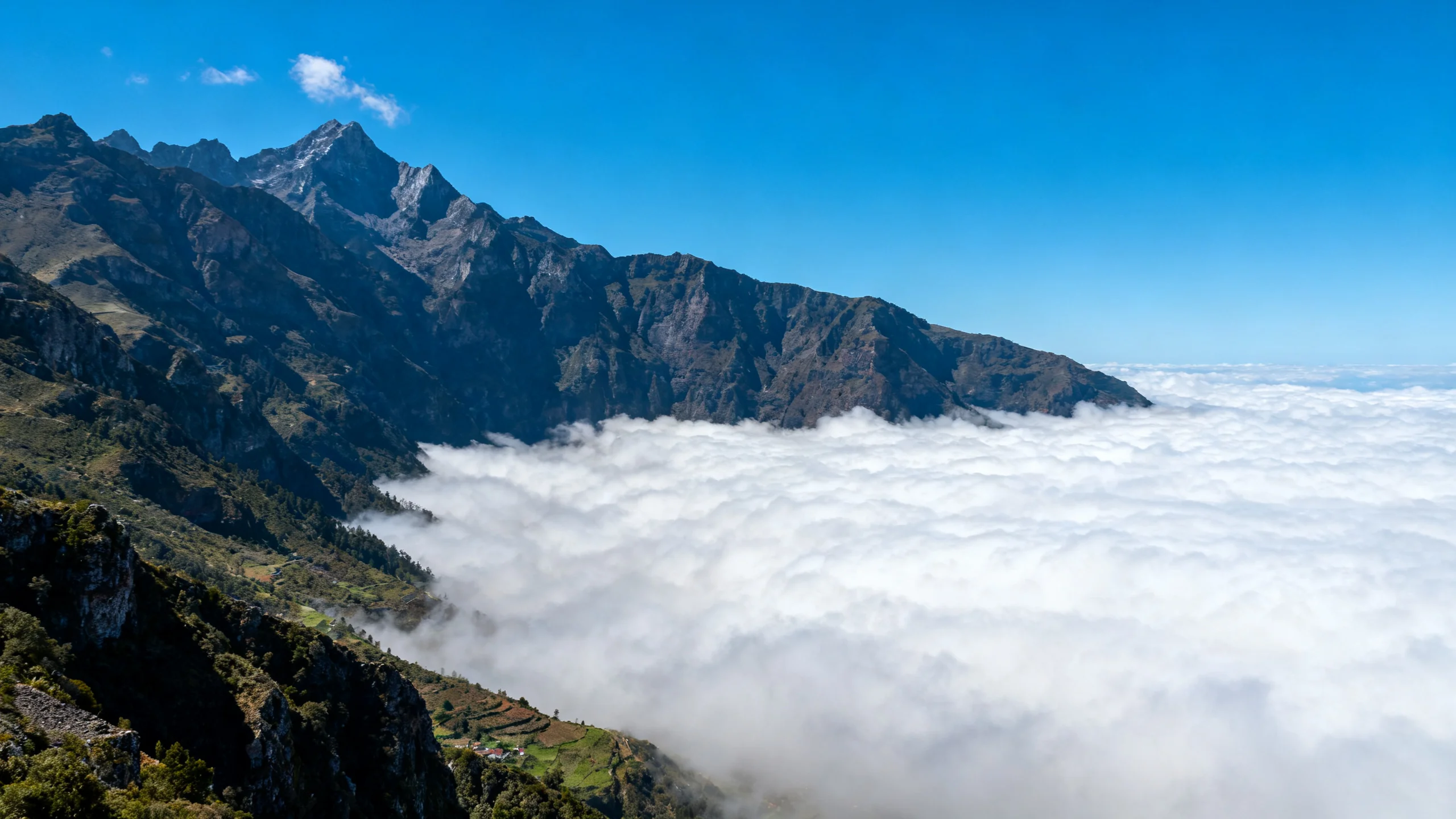 A sea of cloud filling a Madeira valley below a high mountain ridge with blue sky above and the peaks rising clear