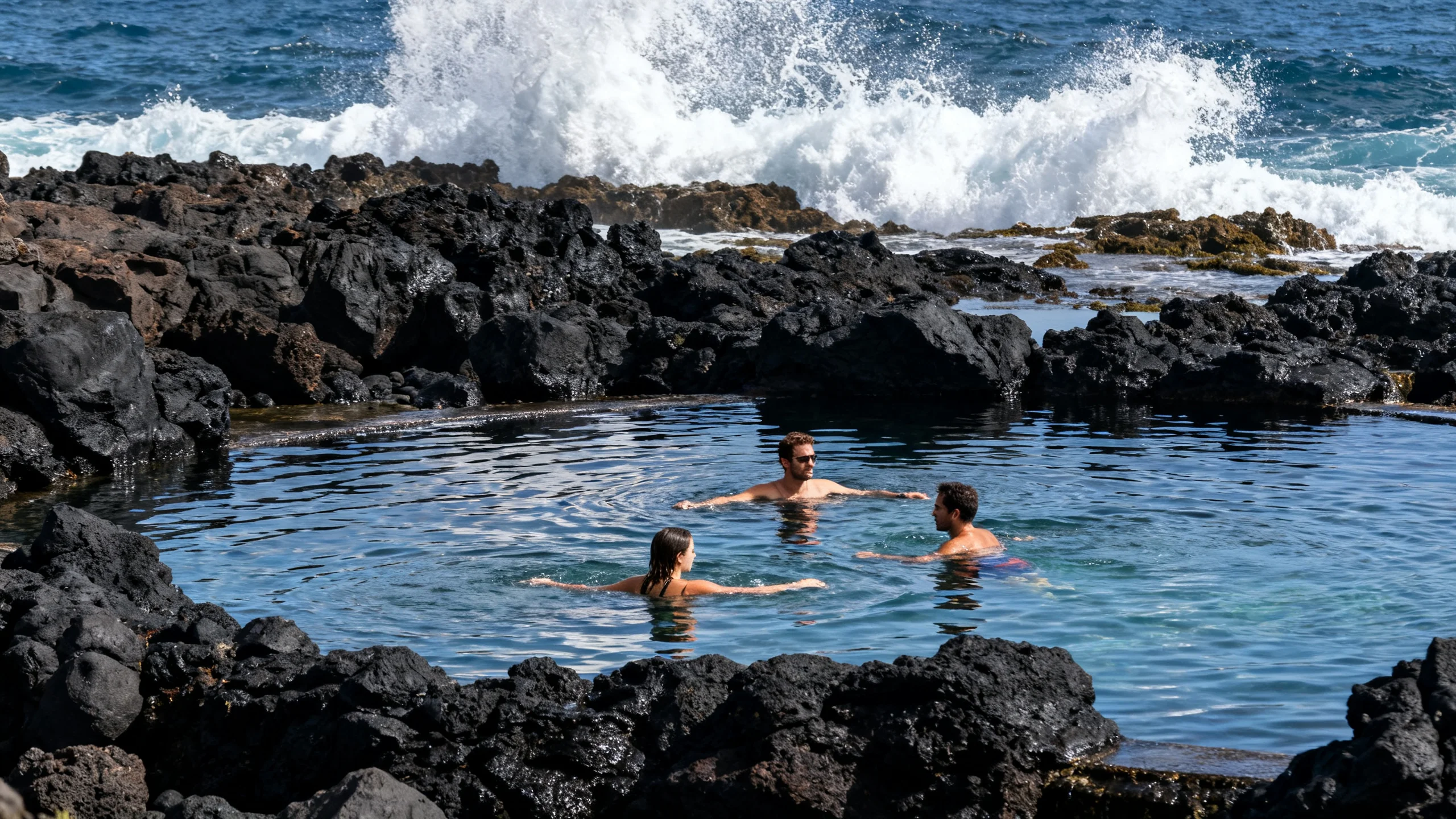 Personas nadando en las piscinas de roca volcánica negra de Porto Moniz con el Atlántico rompiendo contra las rocas al fondo