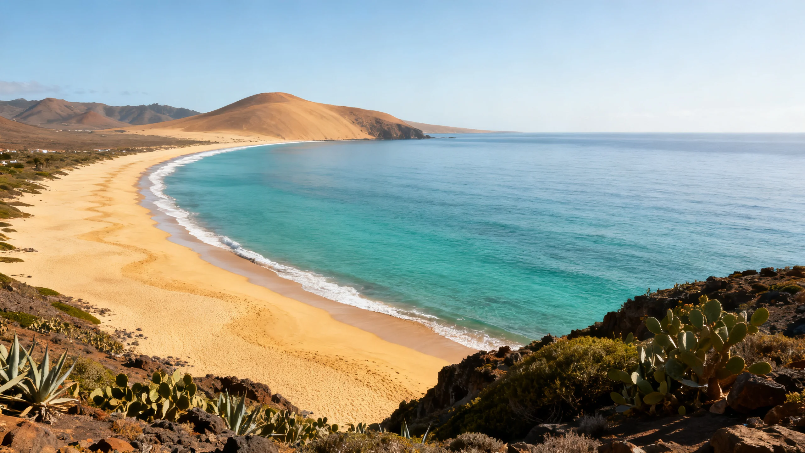 La larga playa de arena dorada de Porto Santo curvándose junto a un mar turquesa tranquilo bajo un cielo despejado